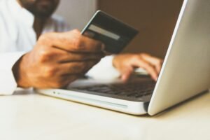 Image of man holding a debit card in front of their computer to make a transaction